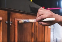 A photo of a hand applying paint to a wooden cabinet