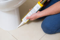 A photo of someone using a caulk gun to seal a toilet