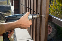 A handyman fixing a fence with a drill